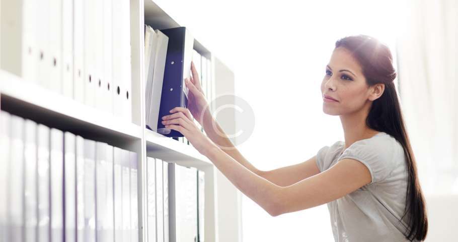 Una mujer está organizando archivos en un estante de una oficina.