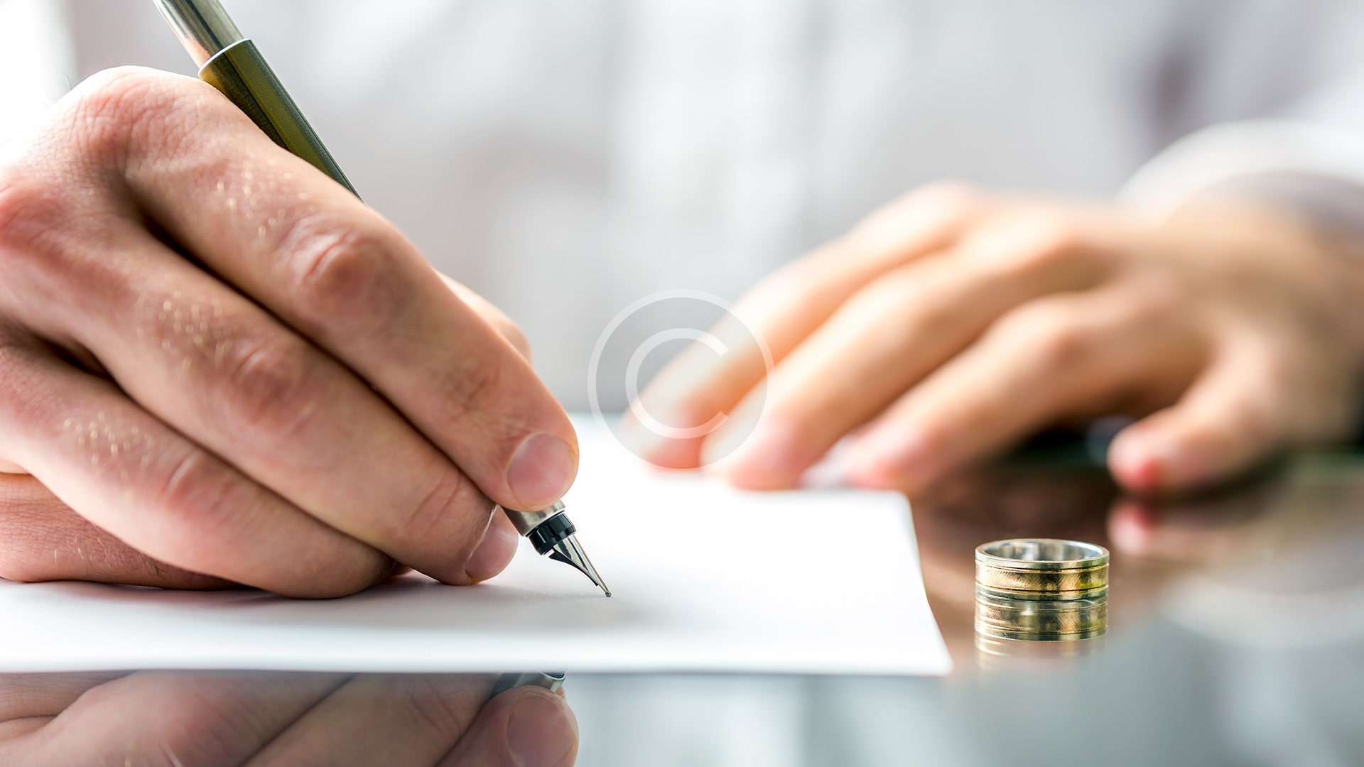 Un abogado de familia firma un documento con un anillo de matrimonio.